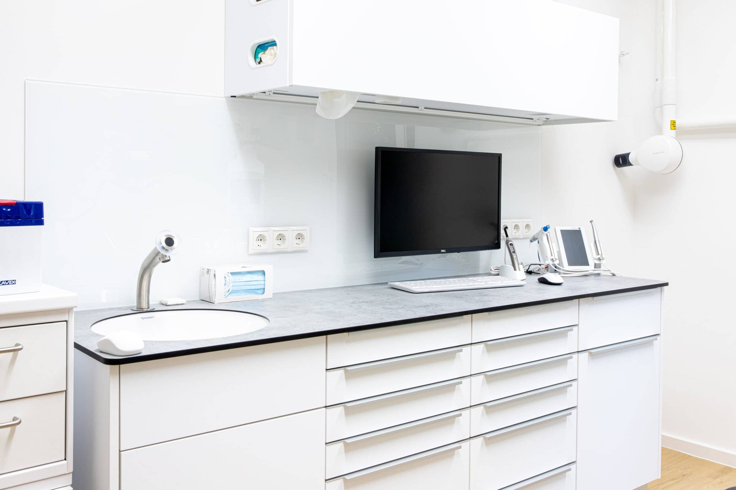 Weiße Behandlungszeile mit Waschbecken, geschlossenen Schubladen und ausgeschaltetem Monitor